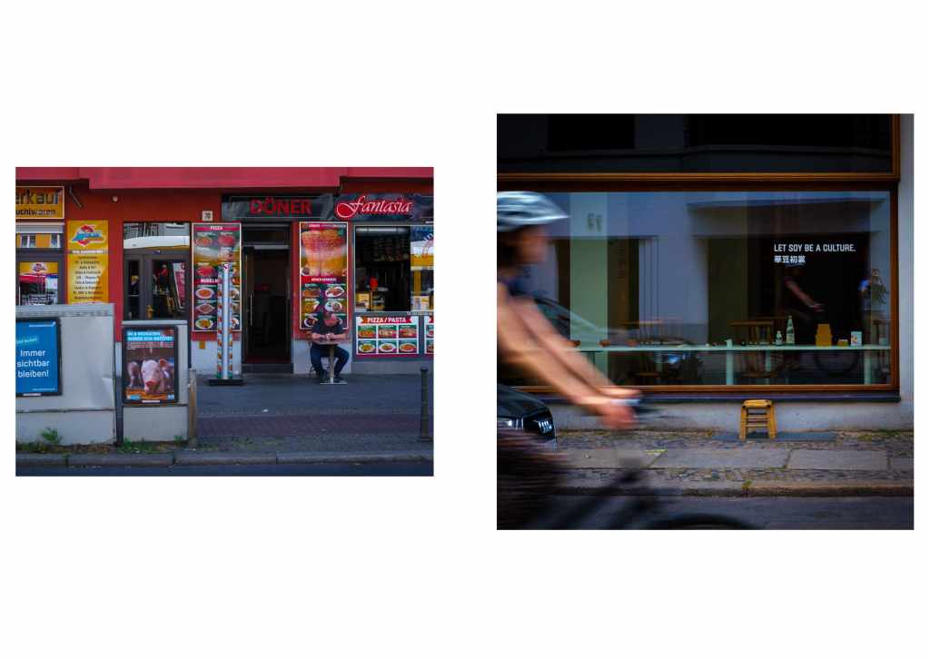 Two photographs. One shows a cafe owner outside a fast food restaurant called Doner Fantasia. The man has a ruddy pink complexion. One can see the street and there are several postes, one is of a pig. In the second photo, a cyclist is travellng past a restaurant window with the sign LET SOY BE A CULTURE and some Chinese lettering. In the window reflection you can see the photographer.