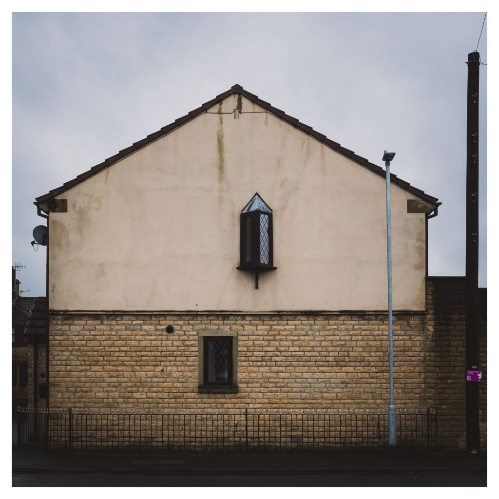 A view of an ordinary house which has a low railing in front of it, a new metal lamp post and a telegraph pole.